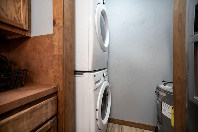 washroom featuring baseboards, cabinet space, water heater, stacked washer and clothes dryer, and a textured wall