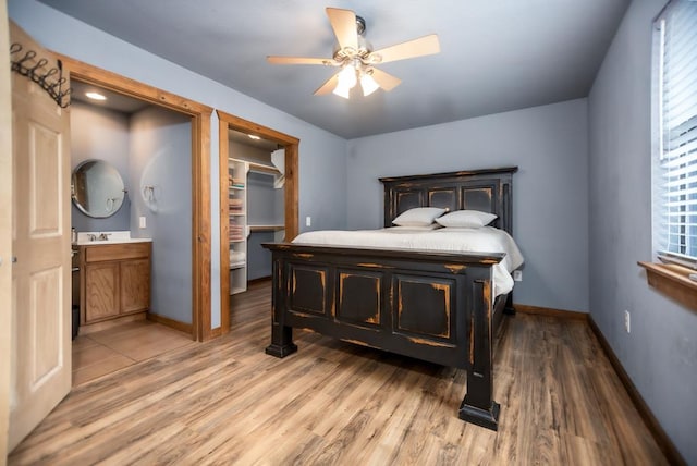 bedroom with a walk in closet, light wood-style floors, baseboards, and a sink