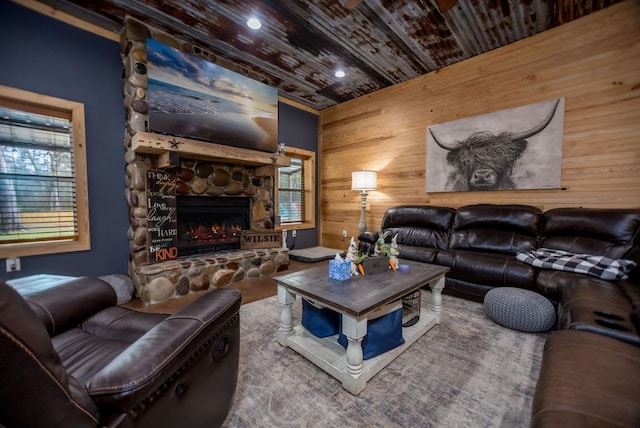 living area with a wealth of natural light, wooden walls, a stone fireplace, and wood ceiling