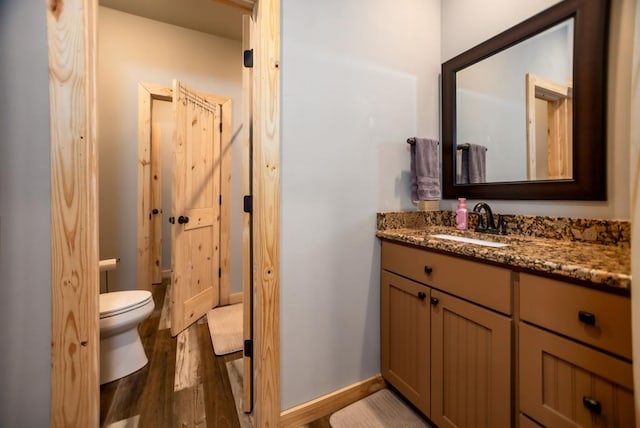 bathroom with toilet, vanity, baseboards, and wood finished floors