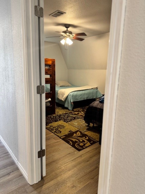 bedroom with lofted ceiling, hardwood / wood-style floors, a textured ceiling, and ceiling fan