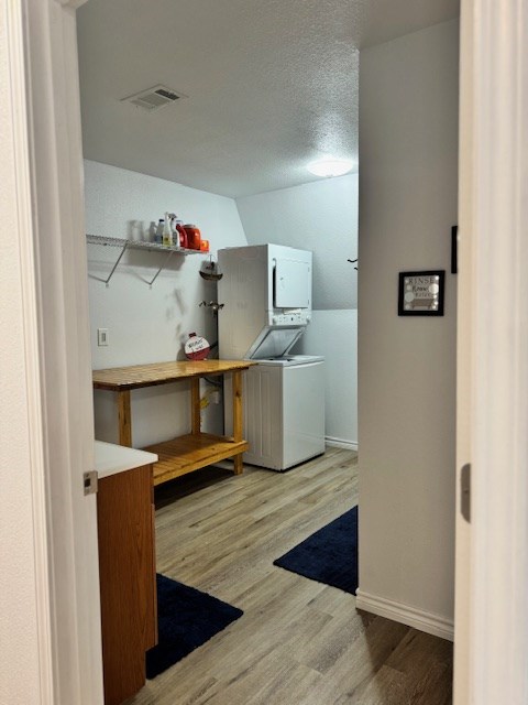 laundry area featuring stacked washer / drying machine, hardwood / wood-style floors, and a textured ceiling