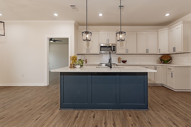 kitchen featuring white cabinetry, stainless steel appliances, tasteful backsplash, hardwood / wood-style floors, and pendant lighting