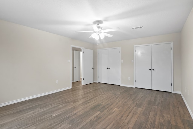 unfurnished bedroom featuring multiple closets, ceiling fan, dark wood-type flooring, and a textured ceiling