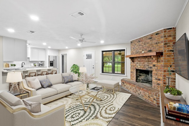 living room featuring a brick fireplace, sink, dark hardwood / wood-style floors, and ceiling fan