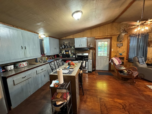 kitchen featuring stainless steel gas range, dark hardwood / wood-style flooring, wood walls, vaulted ceiling, and a kitchen island