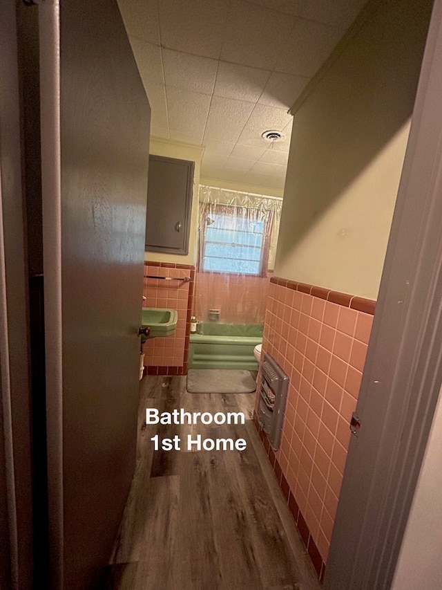 bathroom with tile walls, a tub to relax in, hardwood / wood-style flooring, and sink