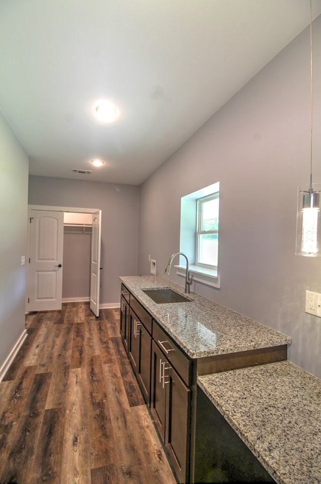 kitchen featuring dark brown cabinets, dark wood-style flooring, light stone counters, a sink, and visible vents