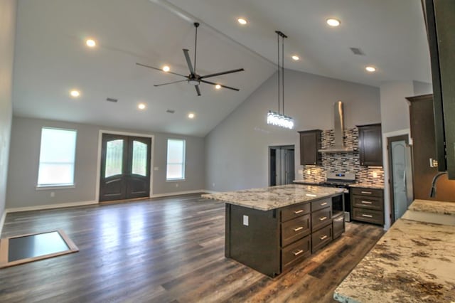 kitchen with ceiling fan, high vaulted ceiling, a center island, wall chimney exhaust hood, and stainless steel range