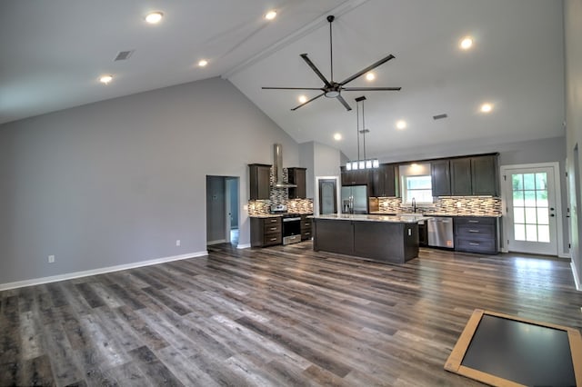 kitchen featuring a kitchen island, appliances with stainless steel finishes, tasteful backsplash, open floor plan, and wall chimney exhaust hood