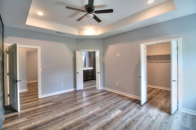 unfurnished bedroom with a walk in closet, visible vents, dark wood finished floors, baseboards, and a tray ceiling