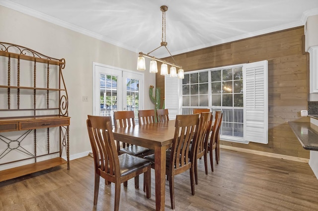 dining room featuring hardwood / wood-style floors, ornamental molding, wooden walls, and an inviting chandelier