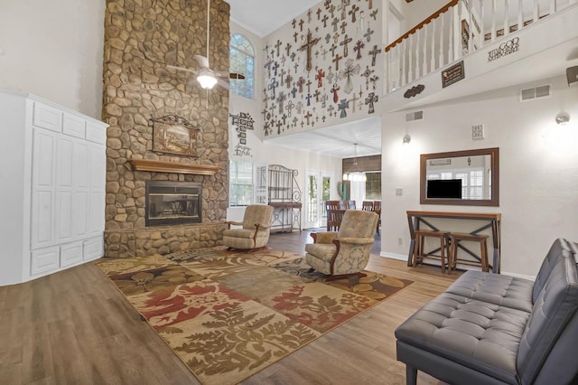 living room with a stone fireplace, ceiling fan, a high ceiling, and light wood-type flooring