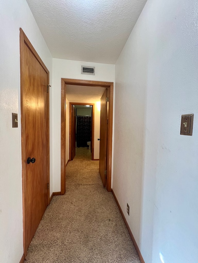 hall featuring a textured ceiling and light colored carpet