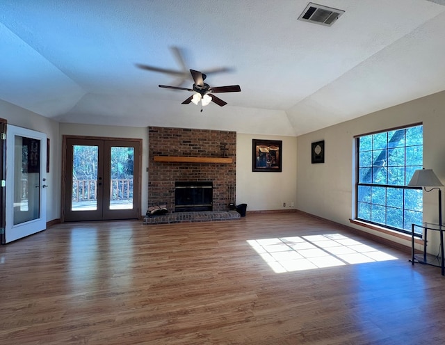 unfurnished living room with light hardwood / wood-style flooring, french doors, lofted ceiling, a fireplace, and ceiling fan