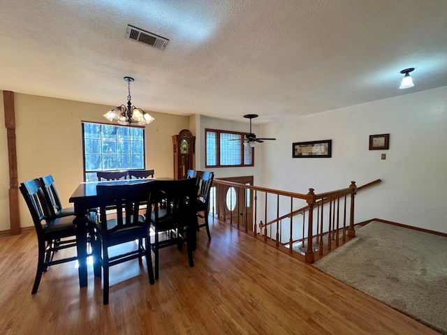 dining room with ceiling fan with notable chandelier, a textured ceiling, hardwood / wood-style floors, and a healthy amount of sunlight