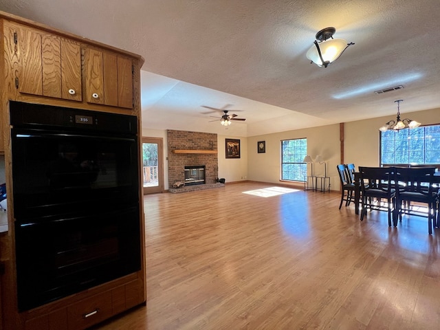 dining area with ceiling fan with notable chandelier, a fireplace, a textured ceiling, and a healthy amount of sunlight