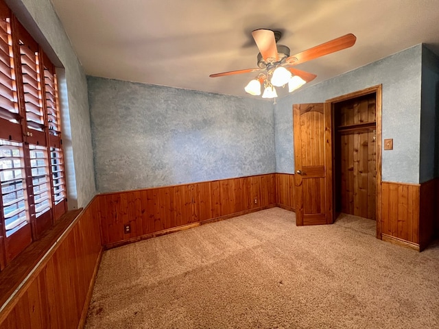 unfurnished bedroom with light carpet, wood walls, and ceiling fan