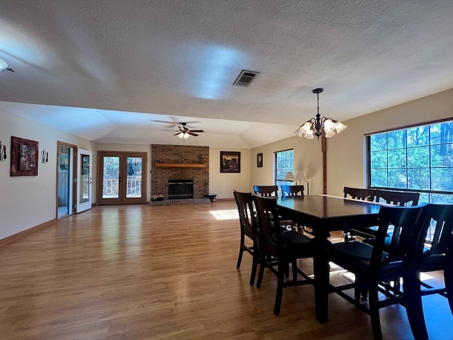 dining room with ceiling fan with notable chandelier, a brick fireplace, french doors, and wood-type flooring