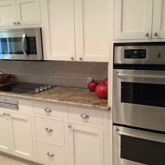 kitchen featuring decorative backsplash, light stone counters, white cabinetry, and appliances with stainless steel finishes