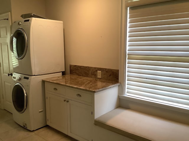 clothes washing area featuring stacked washer and dryer, light tile patterned floors, and cabinets