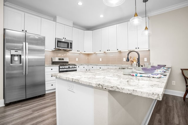 kitchen with wood finished floors, white cabinets, hanging light fixtures, appliances with stainless steel finishes, and crown molding