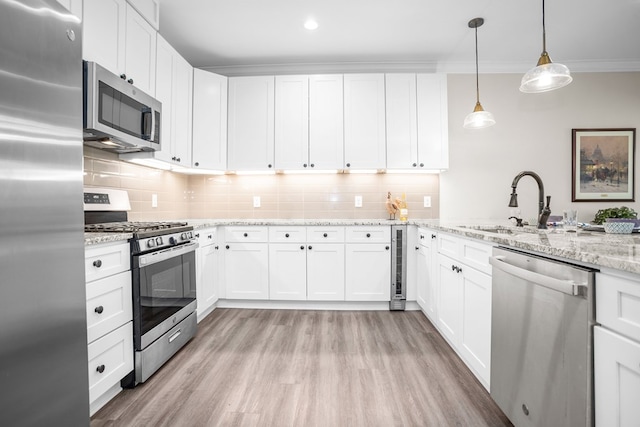 kitchen with white cabinetry, hanging light fixtures, appliances with stainless steel finishes, light stone countertops, and crown molding