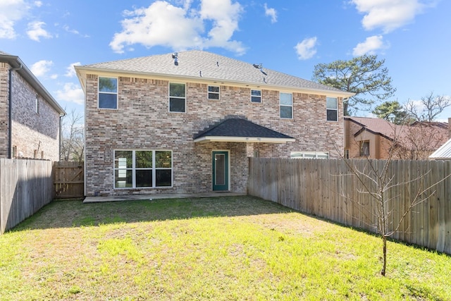 rear view of house featuring a shingled roof, a fenced backyard, a lawn, and brick siding