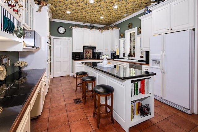 kitchen with white fridge with ice dispenser, ornamental molding, dark countertops, and white cabinetry