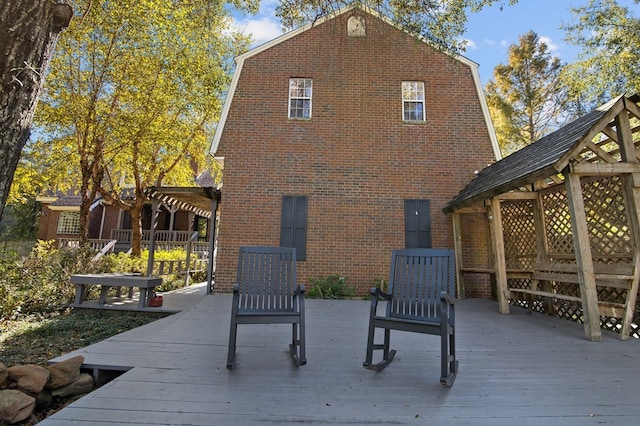 rear view of house featuring brick siding, a deck, a pergola, and a gambrel roof