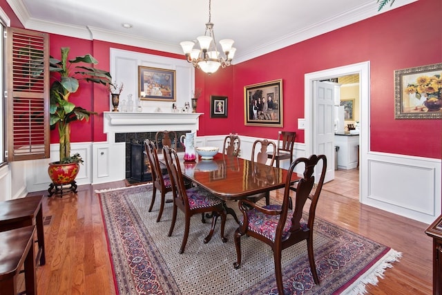 dining area with a tiled fireplace, a wainscoted wall, ornamental molding, wood finished floors, and an inviting chandelier