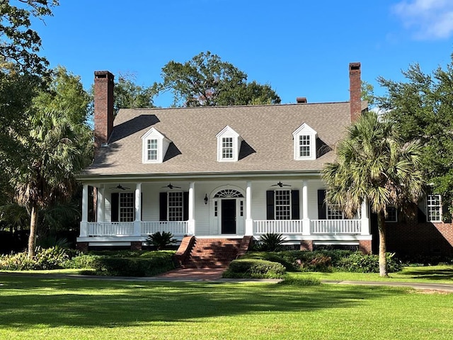 new england style home featuring a porch, a front lawn, a chimney, and a ceiling fan