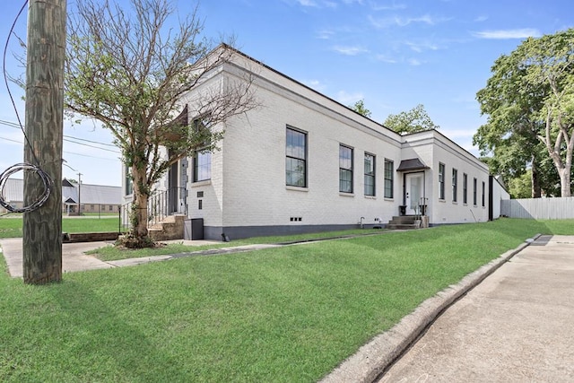 view of side of property with a lawn, fence, and brick siding