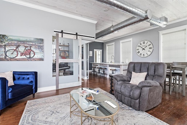 living room with baseboards, a barn door, crown molding, and wood finished floors