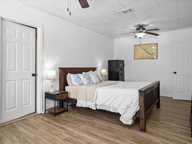 bedroom featuring a ceiling fan, visible vents, and wood finished floors