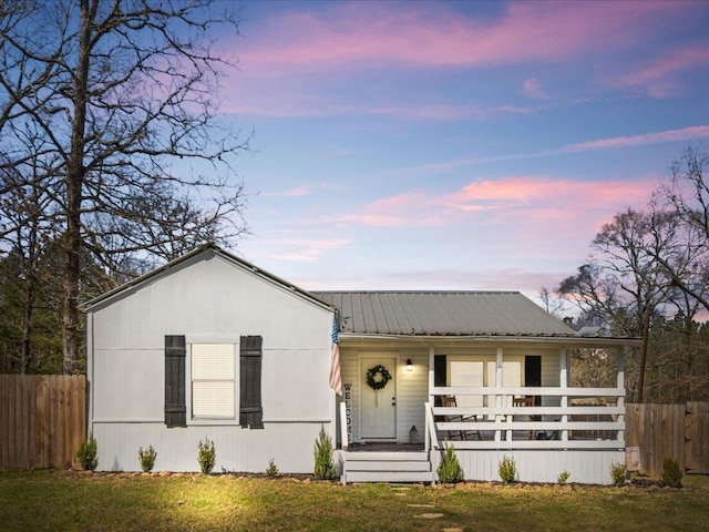 view of front of house with a porch, a front yard, metal roof, and fence