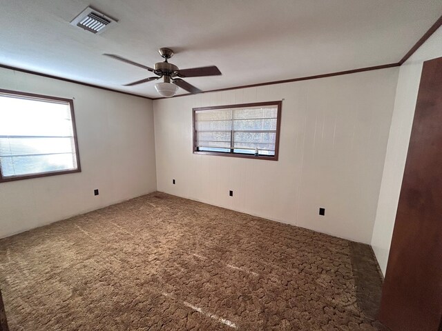 carpeted spare room featuring crown molding, visible vents, and ceiling fan