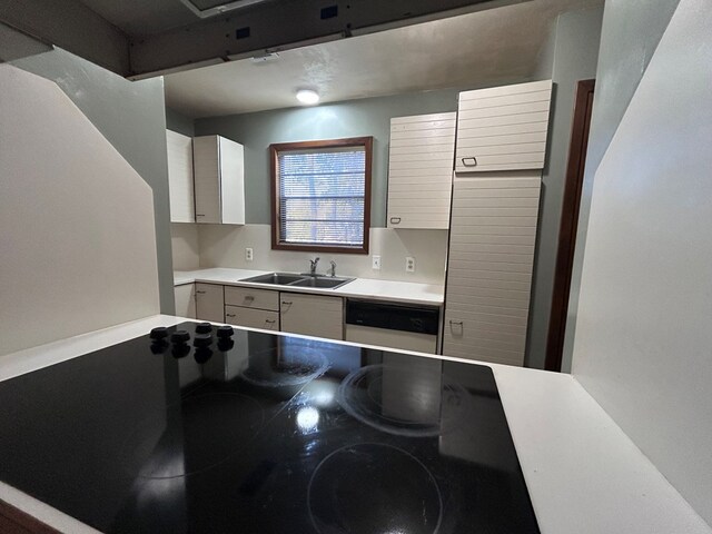 kitchen featuring dishwasher, light countertops, a sink, and white cabinetry