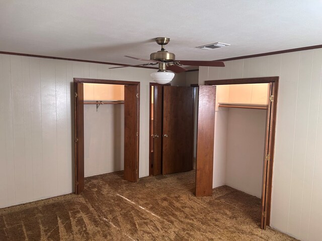 unfurnished bedroom featuring carpet flooring, visible vents, a ceiling fan, ornamental molding, and two closets