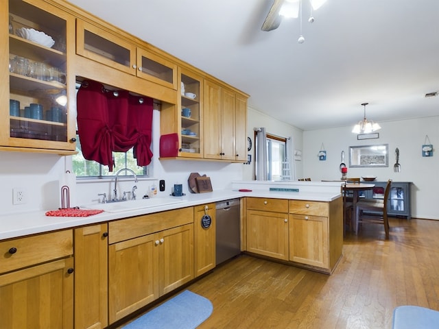 kitchen with kitchen peninsula, stainless steel dishwasher, sink, wood-type flooring, and hanging light fixtures