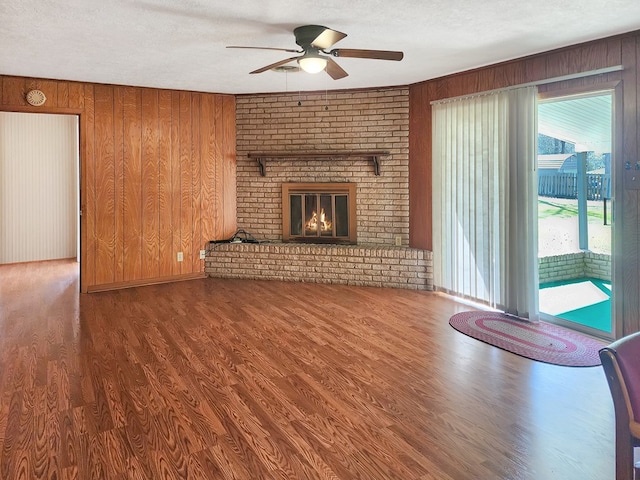 unfurnished living room with ceiling fan, wood walls, a fireplace, wood finished floors, and a textured ceiling