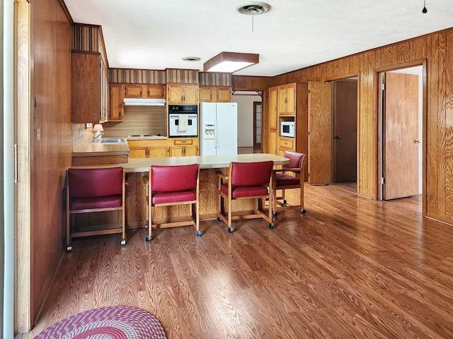 kitchen featuring white appliances, wood finished floors, brown cabinetry, and light countertops