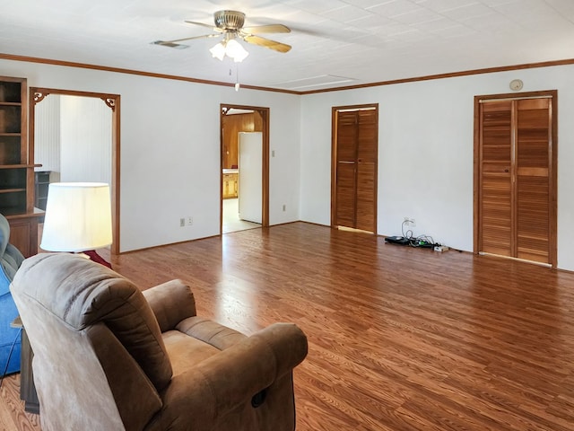 living room featuring ceiling fan, visible vents, wood finished floors, and crown molding