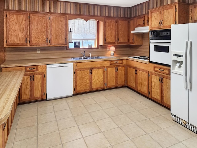 kitchen with a sink, white appliances, brown cabinetry, and light countertops