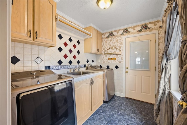 laundry room featuring a textured ceiling, sink, ornamental molding, washer and dryer, and cabinets