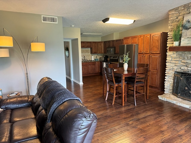 dining area featuring a textured ceiling, a stone fireplace, and dark wood-type flooring