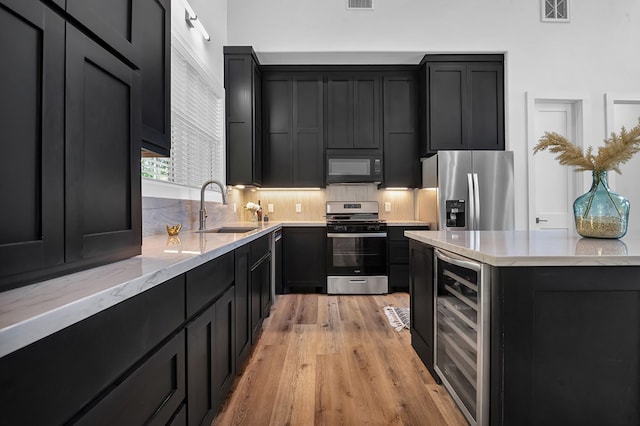 150 Tatanka Trl, Brookeland, TX 75931 - kitchen with stainless steel appliances, a sink, dark cabinetry, wine cooler, and light wood-style floors
