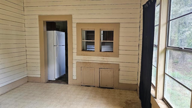 interior space with white refrigerator and wooden walls