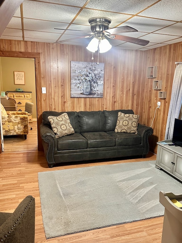 living room featuring wooden walls, a drop ceiling, ceiling fan, and hardwood / wood-style flooring