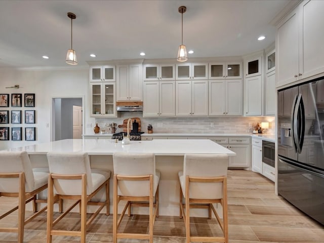 kitchen featuring stainless steel refrigerator with ice dispenser, a kitchen island with sink, decorative light fixtures, white cabinets, and a breakfast bar area